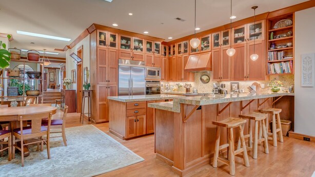 A spacious kitchen with wooden cabinets, a stainless steel refrigerator, and a central island with stools. - Incredible Luxury Loft in Historic Downtown McMinnville (McMinnville)