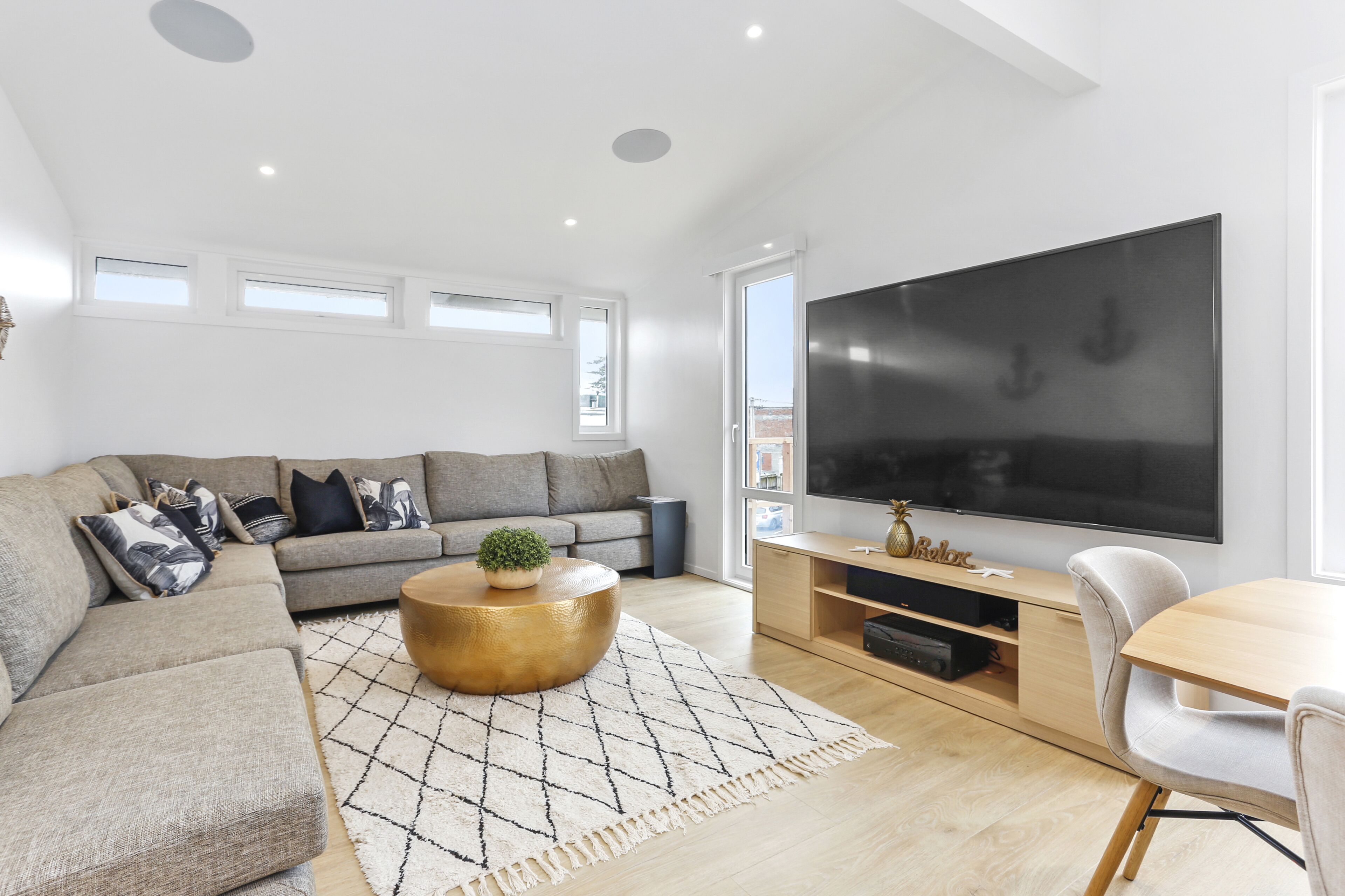 Uma sala de estar moderna com um sofá seccional, uma mesa de centro, uma televisão de tela plana e um espaço de jantar.