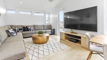 Uma sala de estar moderna com um sofá seccional, uma mesa de centro, uma televisão de tela plana e um espaço de jantar.