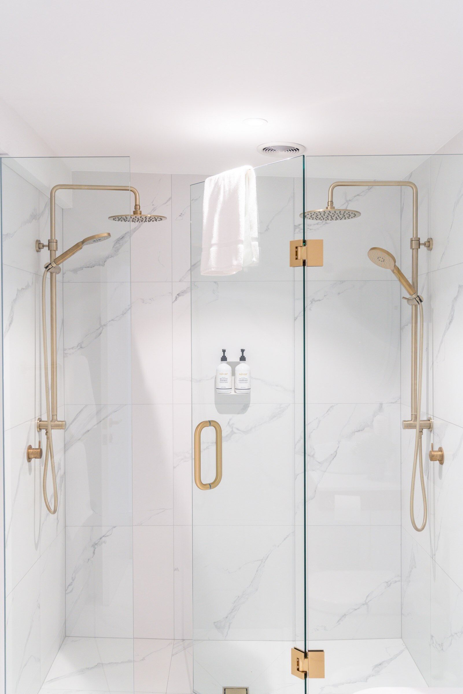A glass-enclosed shower with gold fixtures and marble walls.