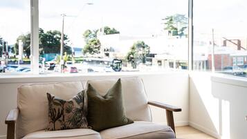 Una habitación con un sofá color beige, una ventana que da a un estacionamiento y edificios.