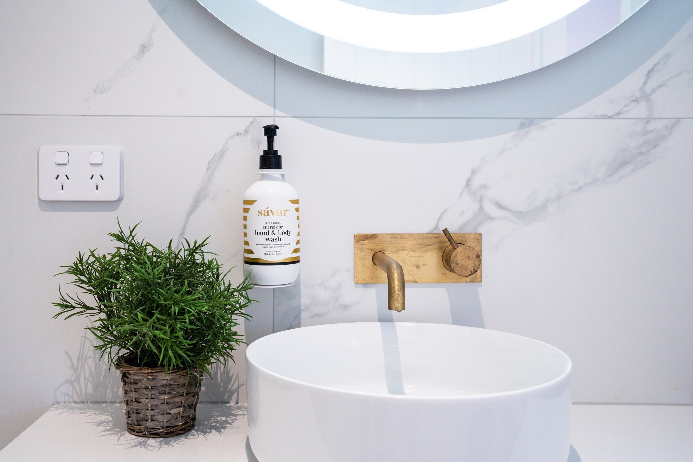 A bathroom with a white marble sink, a wooden towel rack, a potted plant, and a bottle of hand and body wash.