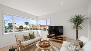 A modern living room with a sofa, TV, and a view of the city. - Stay Mission Bay (Auckland)