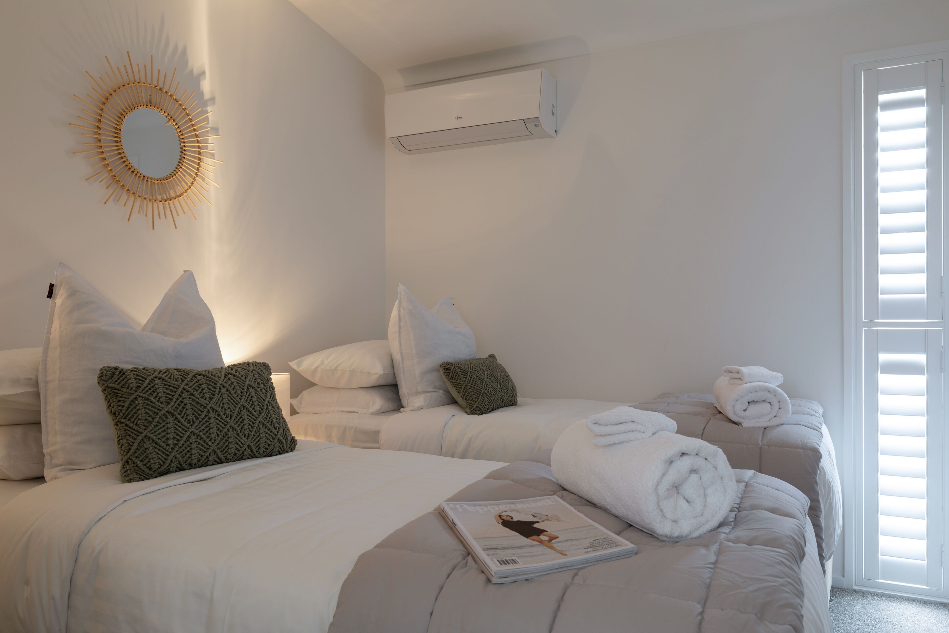 A hotel room with two beds, a wall-mounted air conditioner, a large mirror, and a window with blinds.