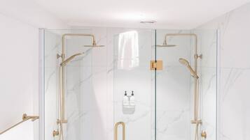 A modern shower with glass doors, gold fixtures, and a towel hanging on the door.