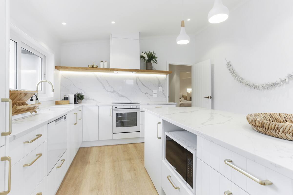 A modern kitchen with white cabinetry, a marble countertop, a built-in oven, and a wooden floor.