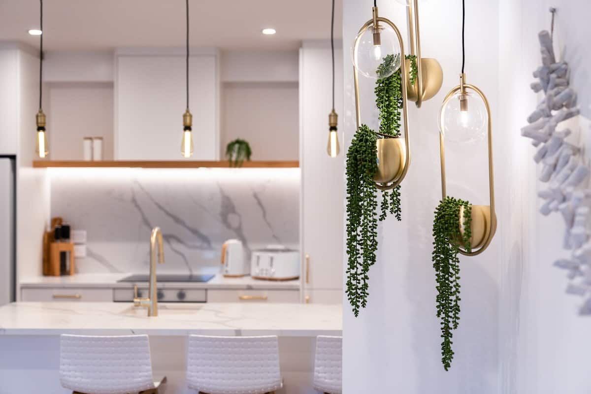 A modern kitchen with white cabinetry, a marble backsplash, and hanging pendant lights with plants.