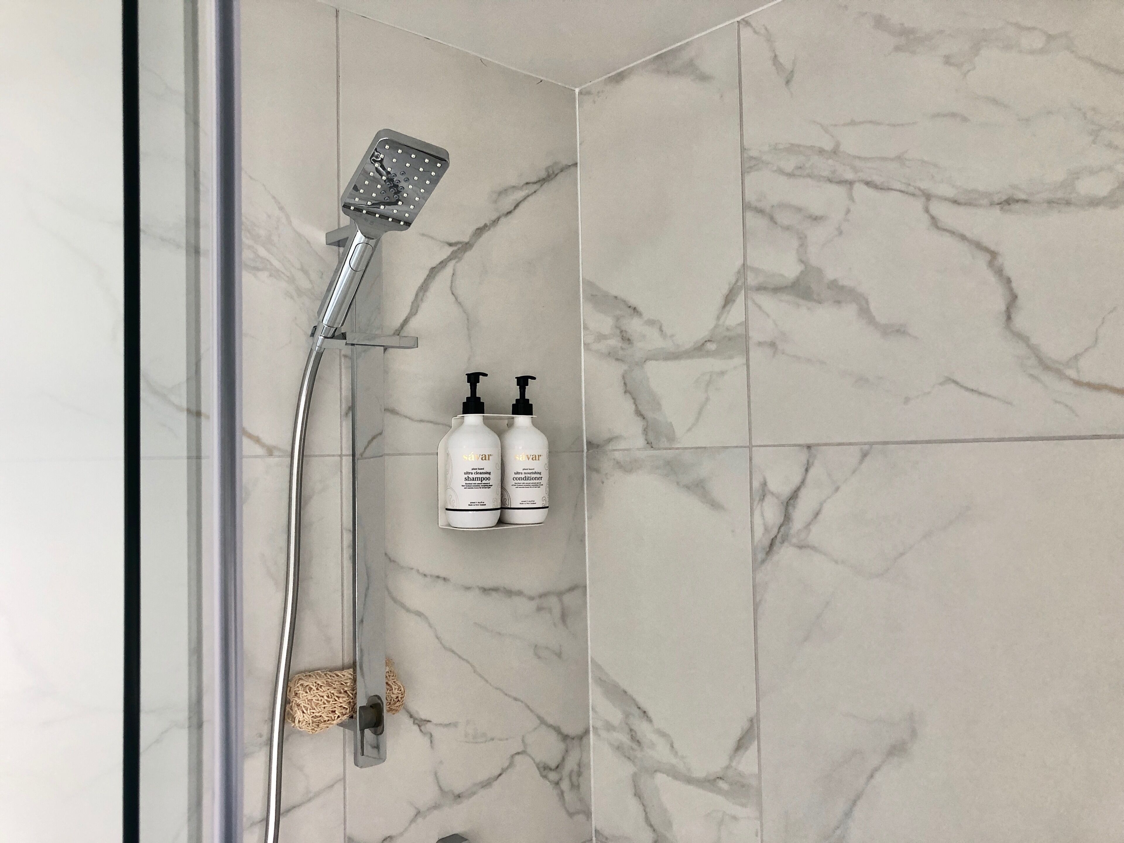 A bathroom with a shower, marble tiles, and two bottles of shampoo and conditioner.