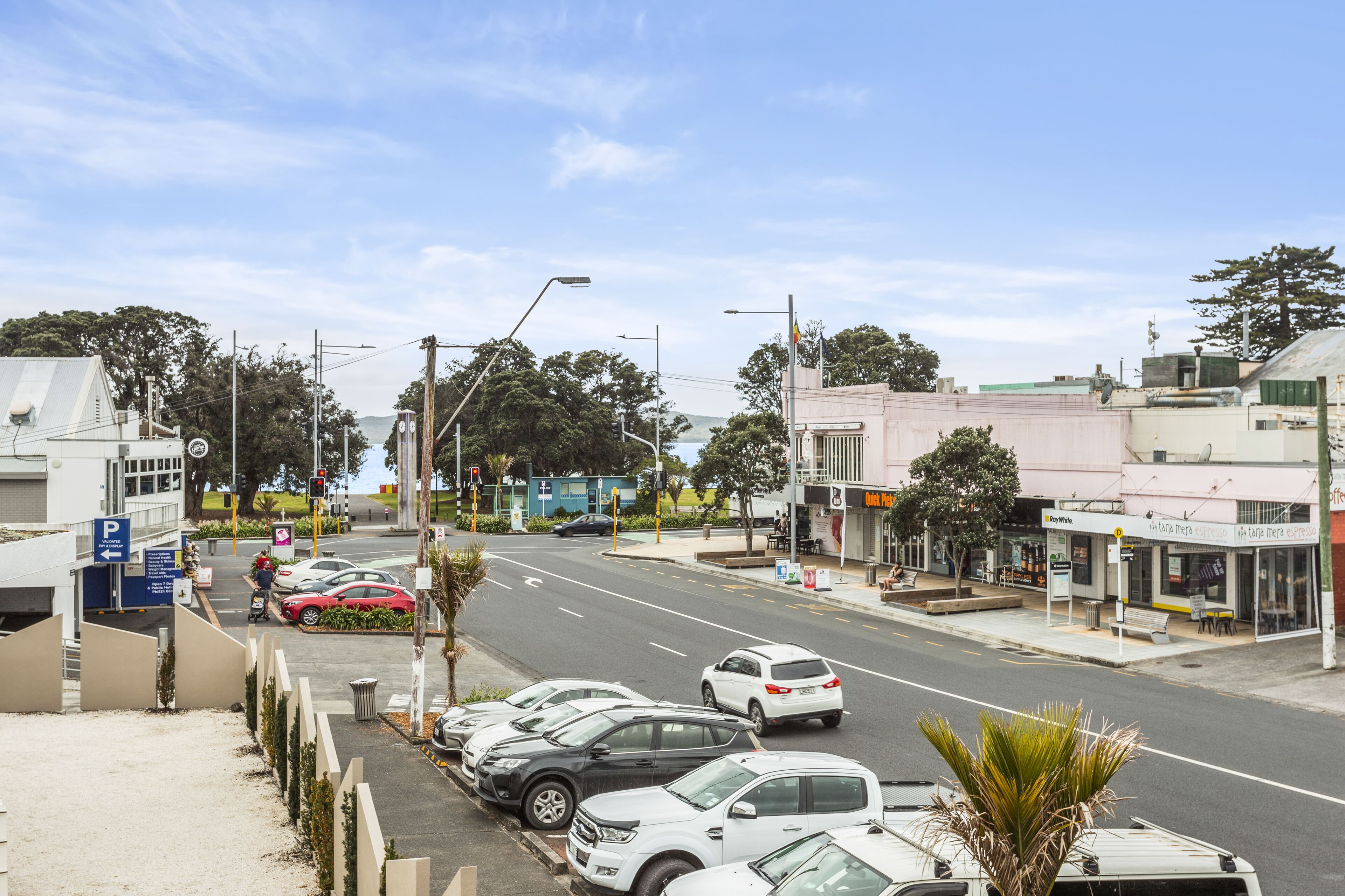 A street view with parked cars, a pedestrian crossing, and buildings with signage.