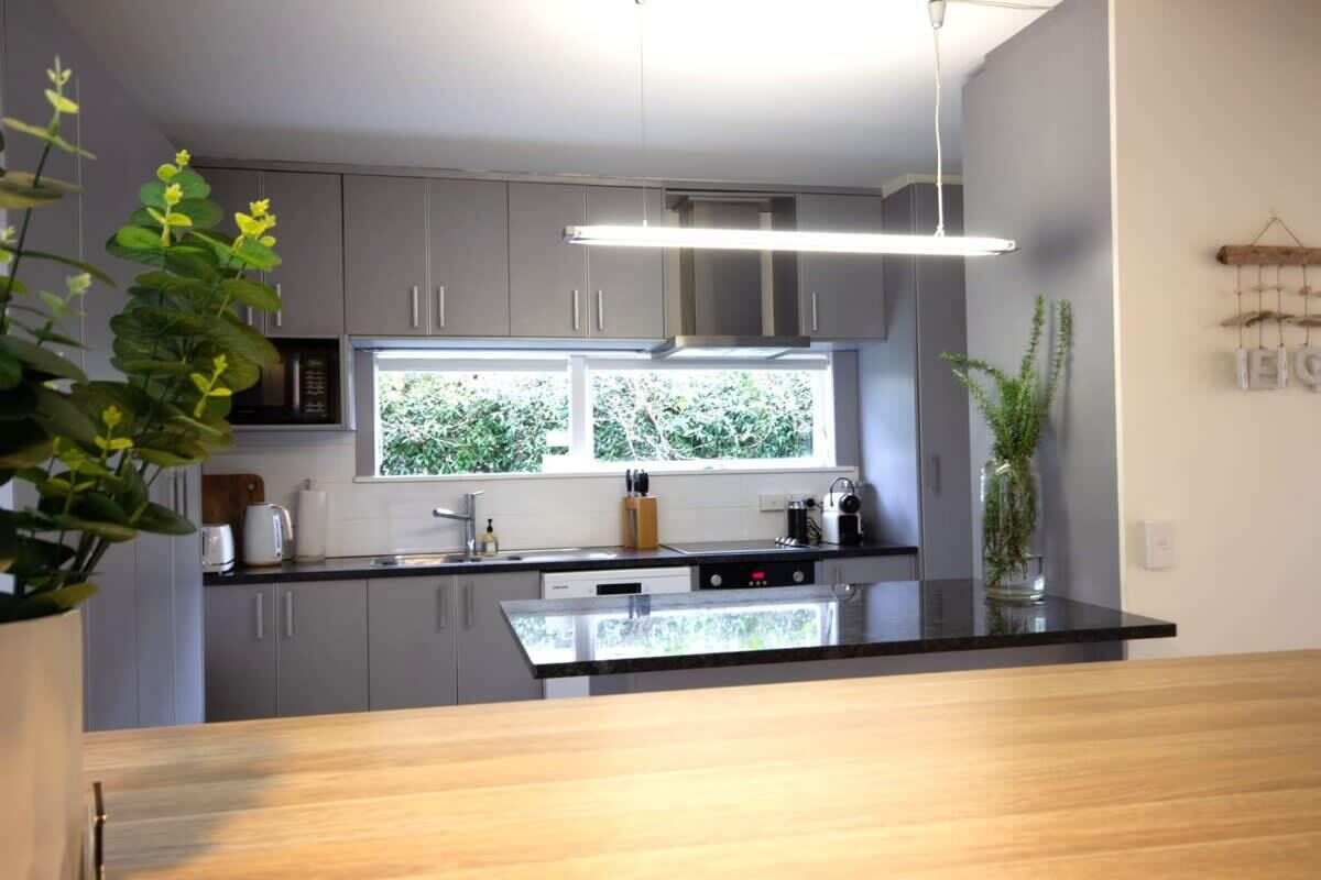 Une cuisine moderne avec des meubles gris, un plan de travail noir et une fenêtre donnant sur un espace verdoyant.