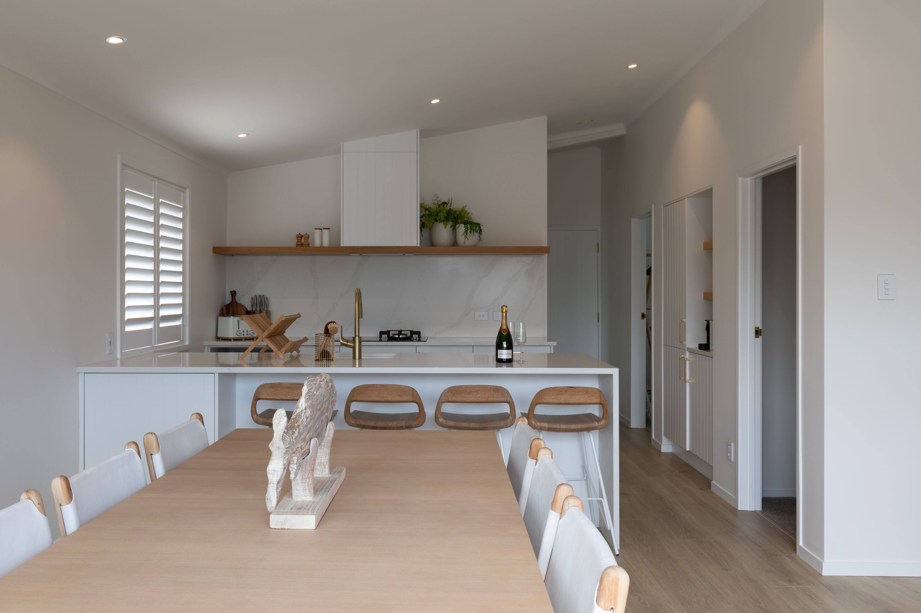Une cuisine moderne dotée d’un îlot central, de meubles blancs et d’un coin repas avec une table et des chaises en bois.