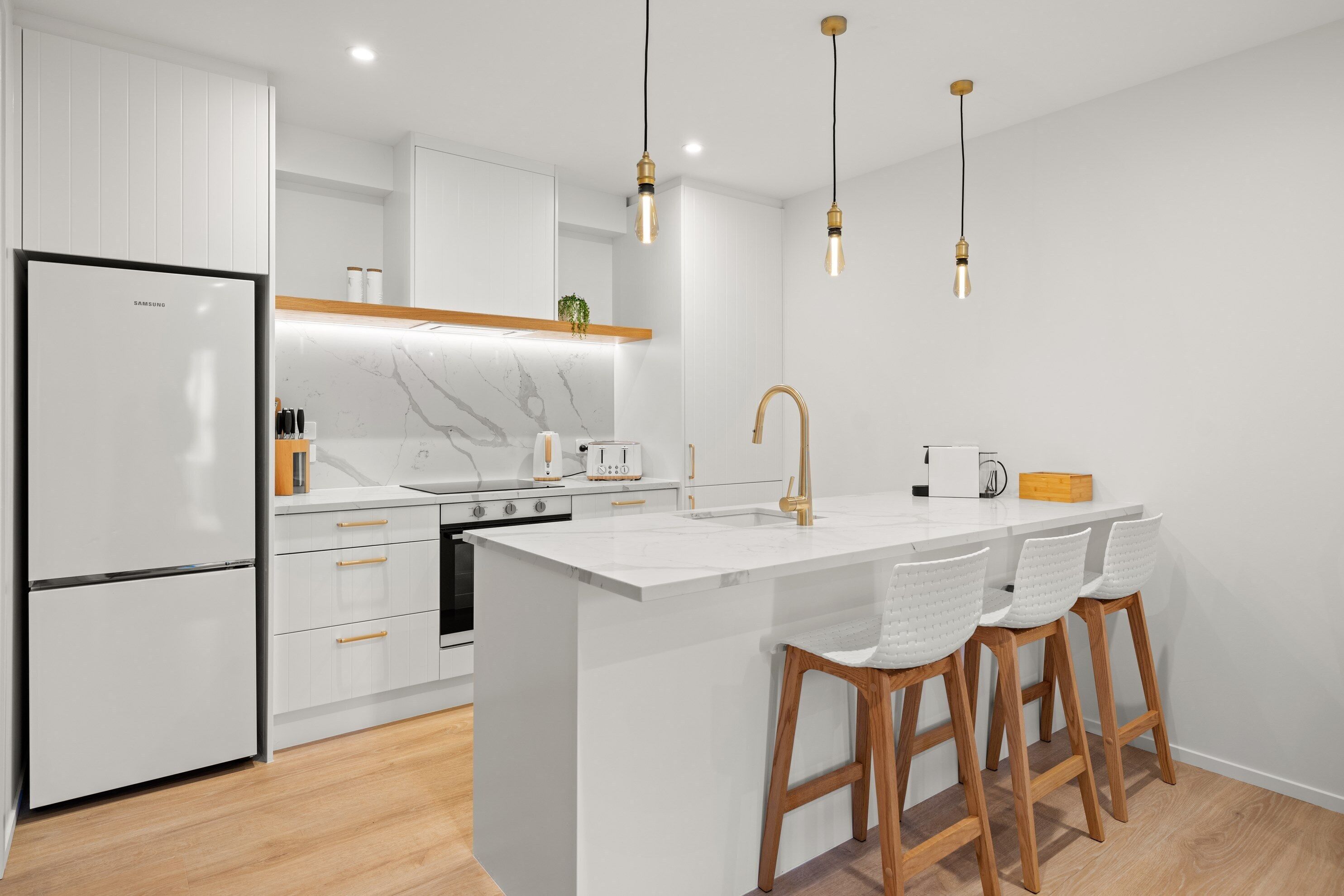 A modern kitchen with a large island, white cabinetry, and wooden stools.