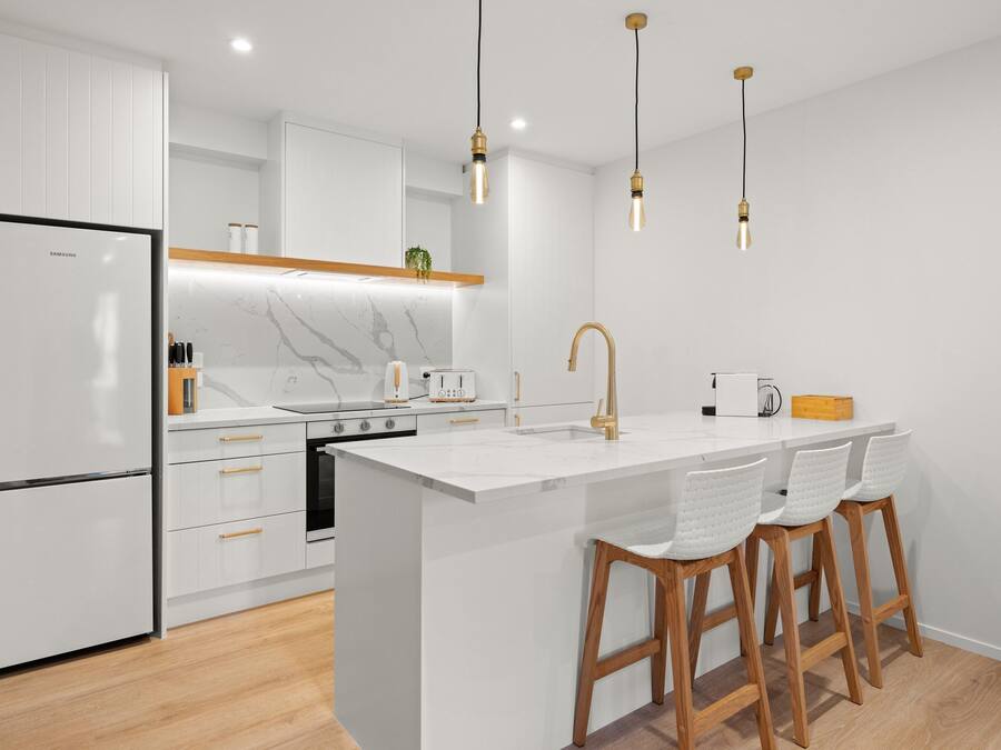 A modern kitchen with a large island, white cabinetry, and wooden stools.