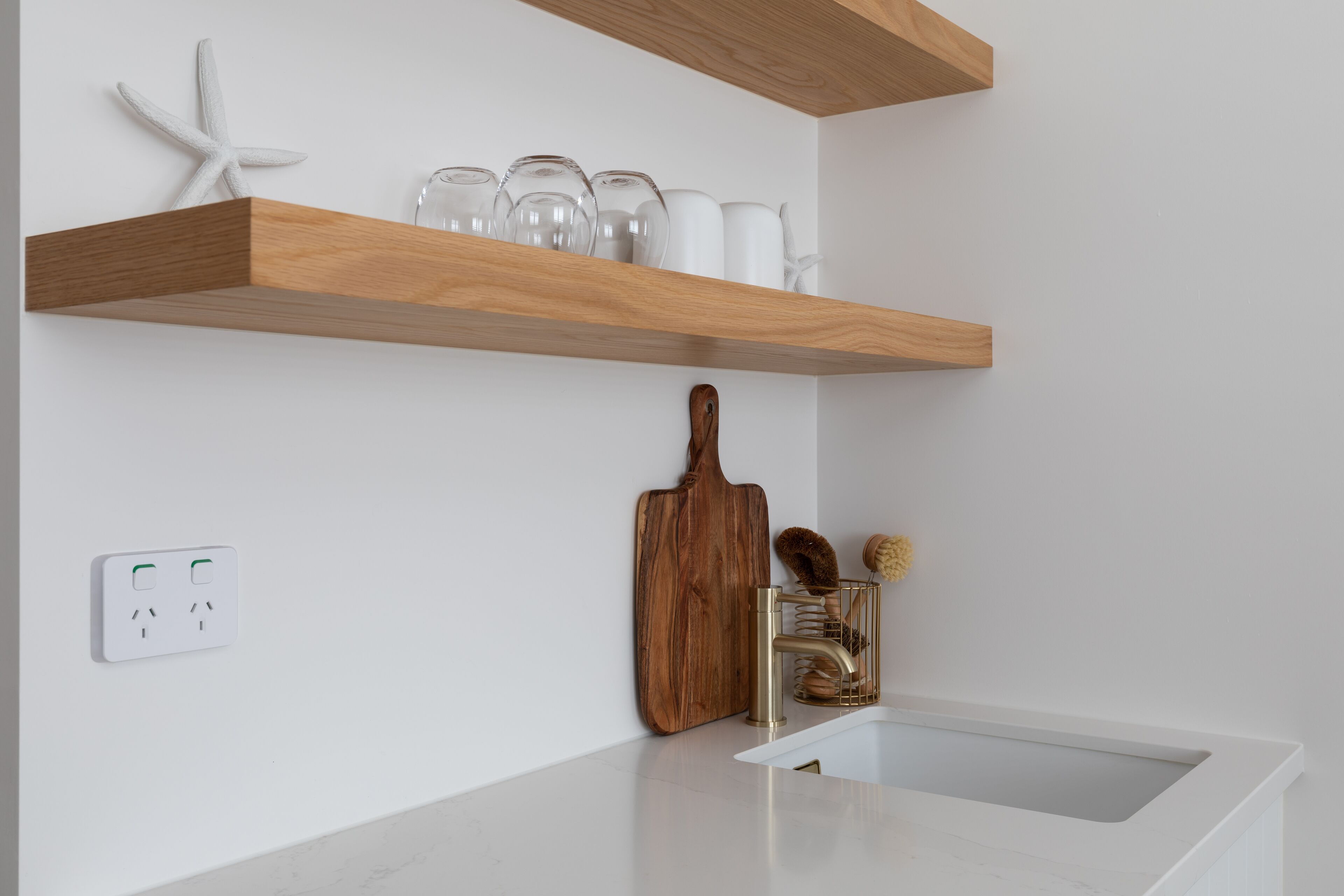 A modern kitchen with a white countertop, a wooden shelf above the sink, and a starfish decoration.