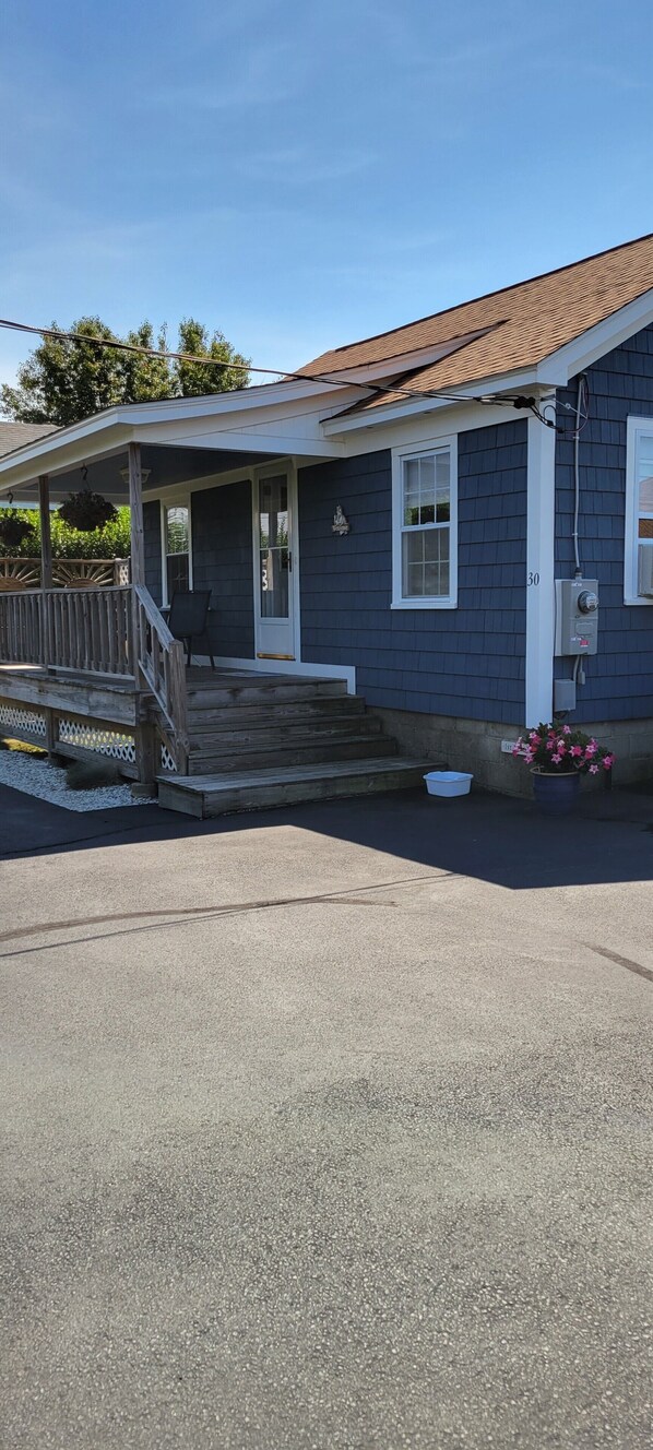 A house with a covered porch, a front door, and a small garden with flowers. - Adorable Cottage Walk Across Street to First Beach, Winter min stay 9 mos (Middletown)