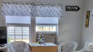 Uma sala de estar com uma mesa de centro de madeira, cadeiras de vime, um sofá e uma TV sobre um móvel.