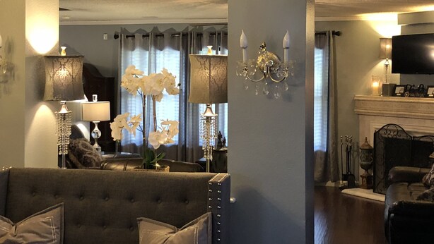 Un salon avec un canapé gris, un lustre et une cheminée.