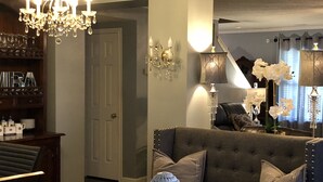 Un salon avec un canapé gris, un lustre et un escalier en arrière-plan.