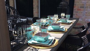Un espace extérieur aménagé pour les repas, avec une table en bois dressée avec de la vaisselle turquoise et marron, entourée de chaises en osier.