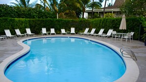 Une piscine dont la profondeur est indiquée à 6 pieds, entourée de chaises longues blanches et d’une haie.