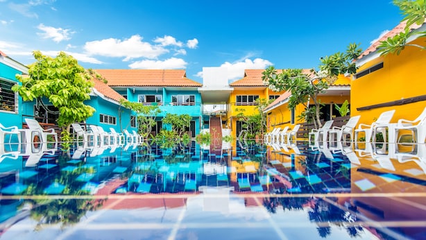A swimming pool with white lounge chairs, surrounded by colorful buildings with a clear blue sky. - PK Resort Pattaya (Pattaya)
