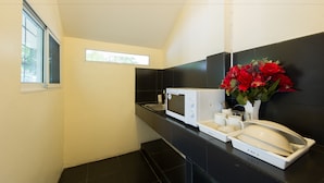 A compact kitchen with a microwave, sink, and a vase of red flowers. - PK Resort Pattaya (Pattaya)
