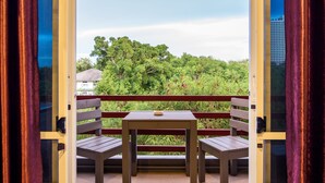 A balcony with a wooden table and two chairs, overlooking a lush green landscape with trees and a building in the background. - PK Resort Pattaya (Pattaya)