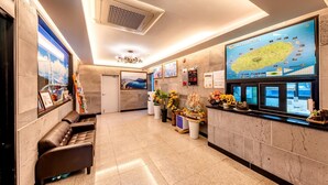 A hotel reception area with a large digital map, a seating area with a sofa, and a decorative plant arrangement. - Chilsimni Hotel (Seogwipo)