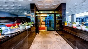 A modern lobby with a car parked outside, a reception desk with potted plants, and a glass door leading to the interior. - Chilsimni Hotel (Seogwipo)