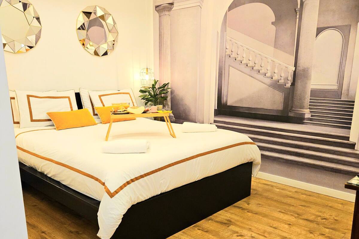 Un dormitorio moderno con una cama grande, piso de madera y vista a un arco arquitectónico.