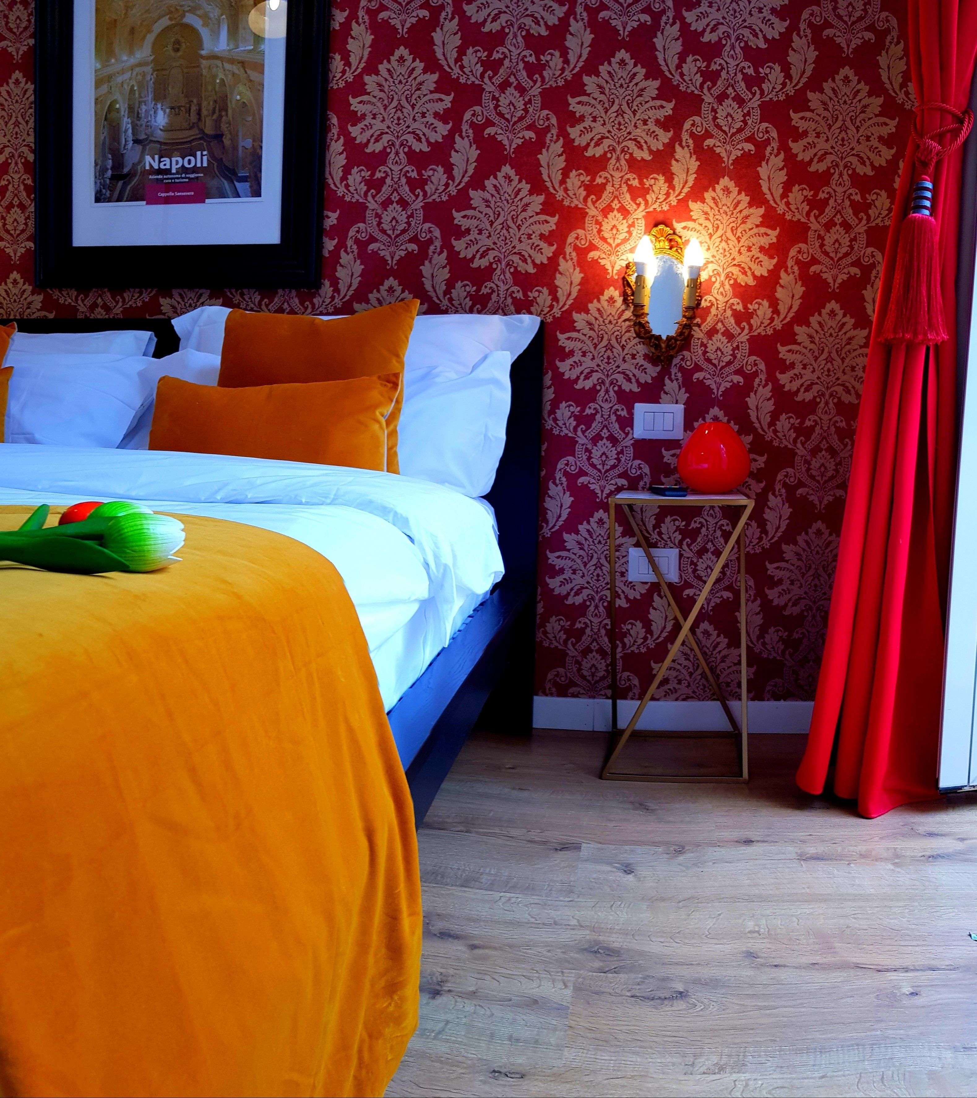 Una camera d'albergo con un letto, un comodino, una tenda rossa e un quadro appeso al muro.