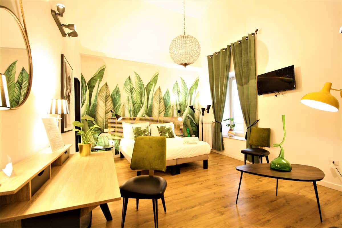 Habitación de hotel con cama, escritorio, silla, mesa, televisor y pared cubierta de plantas.