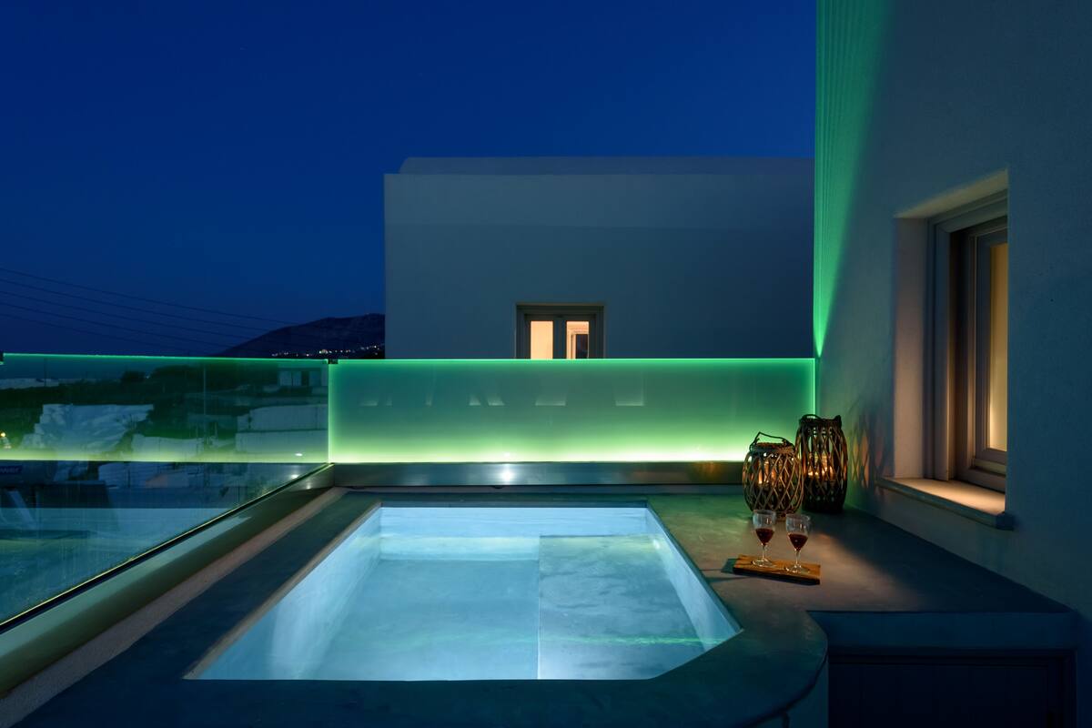 A modern rooftop terrace with a glass-enclosed hot tub, a view of the cityscape, and ambient lighting.