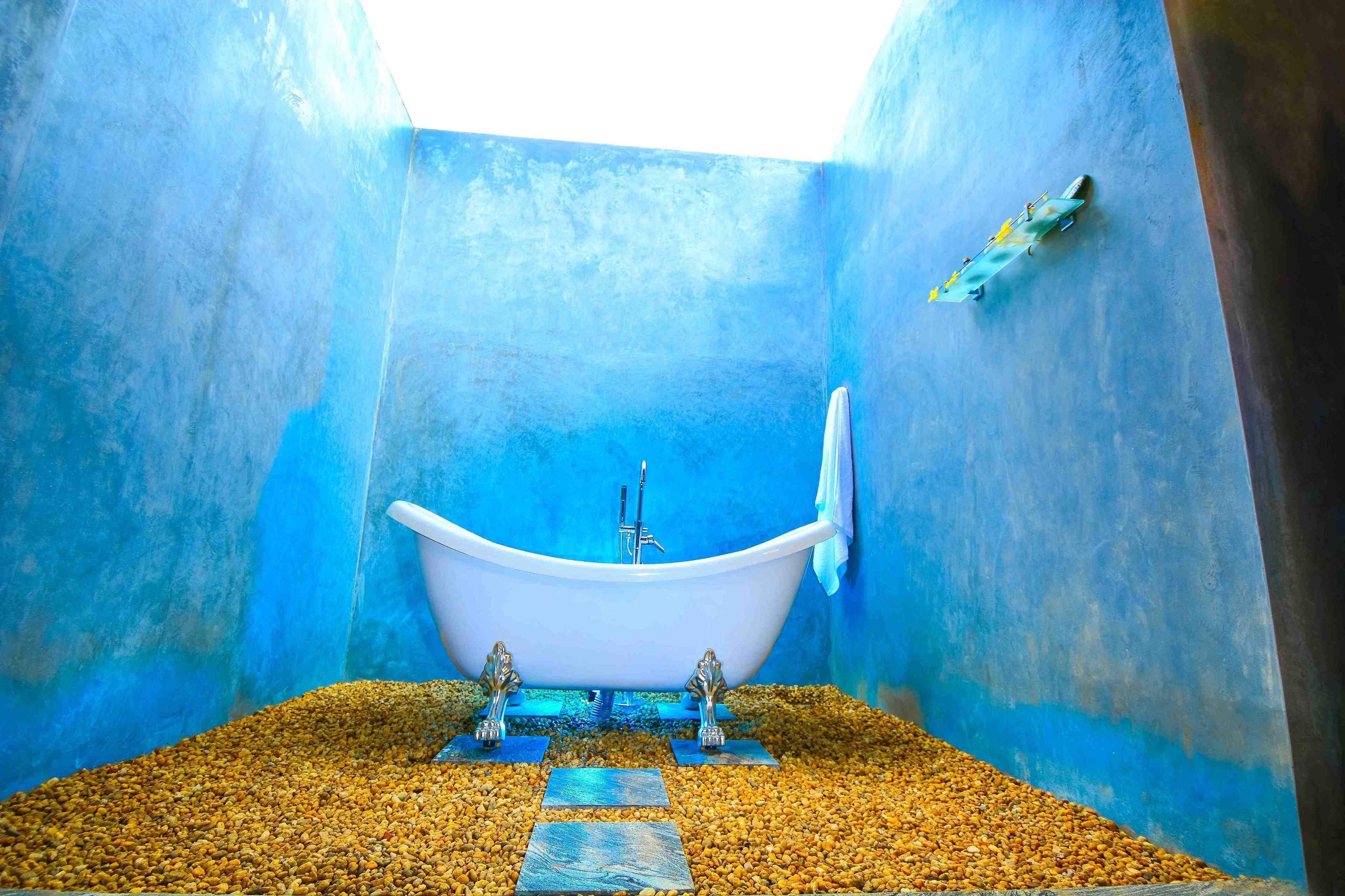 A bathtub in a room with blue walls and a pebble floor.