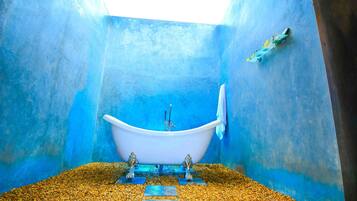 A bathtub in a room with blue walls and a pebble floor.