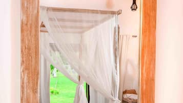 A bedroom with a canopy bed, a wooden-framed mirror, a bedside table with a basket of flowers, and a small table with two mugs.