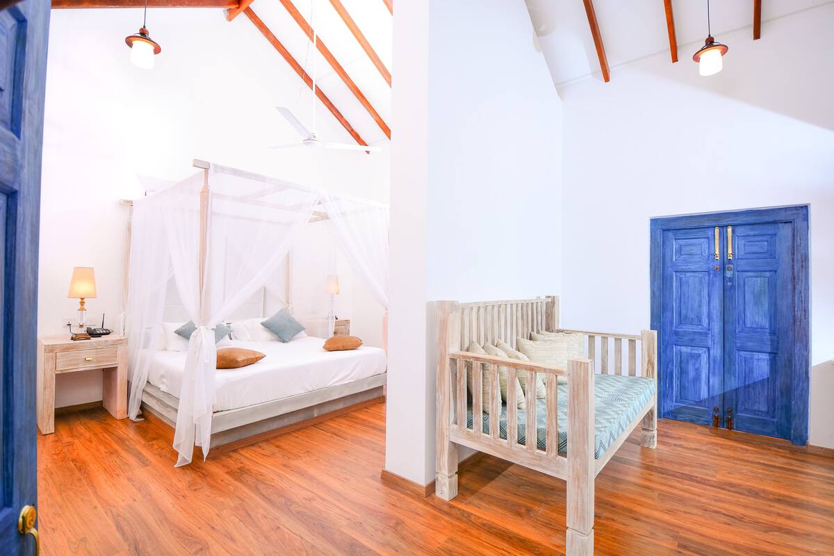A bedroom with a canopy bed, a wooden desk, and a blue door.