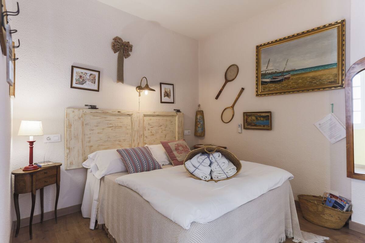 Un dormitorio con cama, mesita de noche, lámpara y adornos de pared, incluyendo un cuadro y fotografías enmarcadas.
