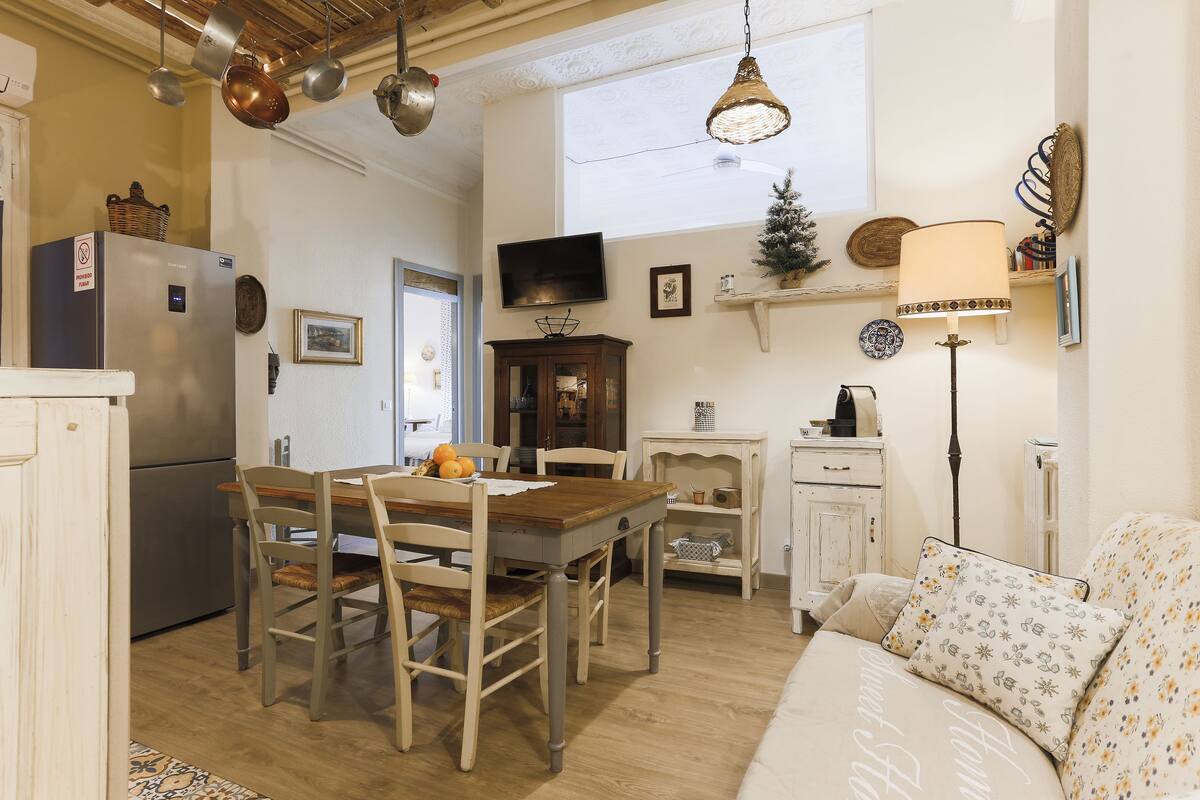Una cocina acogedora con una mesa de comedor, sillas, un refrigerador, un televisor y un pequeño árbol de Navidad.