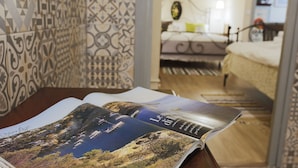 An open magazine on a wooden table with a patterned wall and a bed in the background. - Live in Chianti (Valencia)