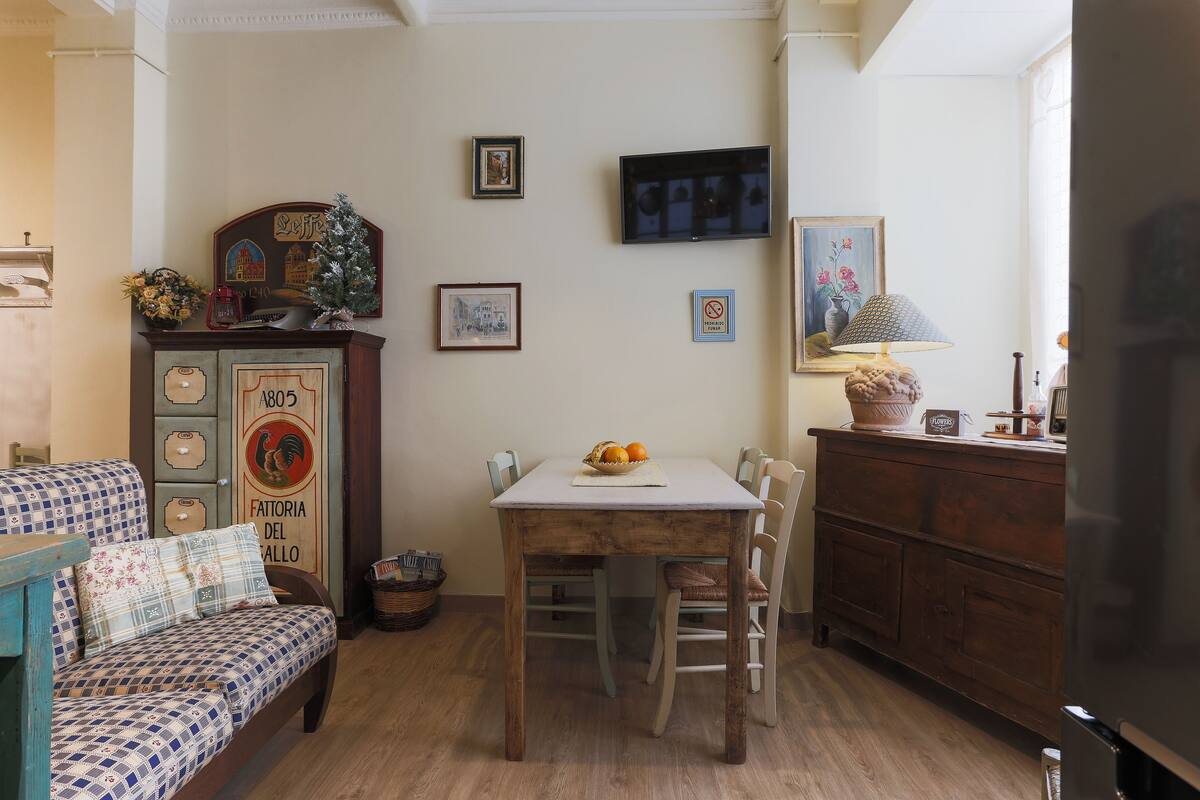 Un comedor con una mesa y sillas de madera, un sofá con cojines estampados y un aparador antiguo con adornos.