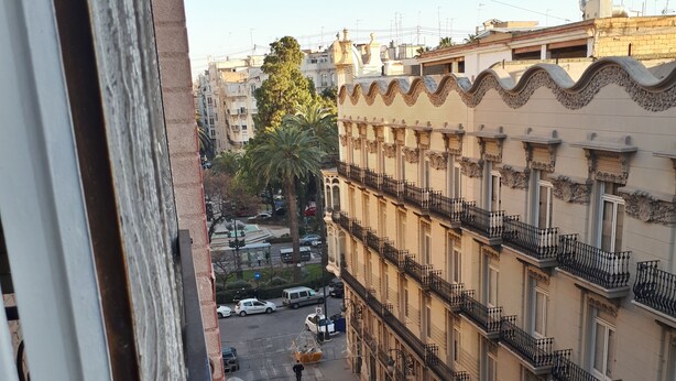 A balcony with red flowers, a view of a street with parked cars, and buildings with balconies. - Live in Chianti (Valencia)