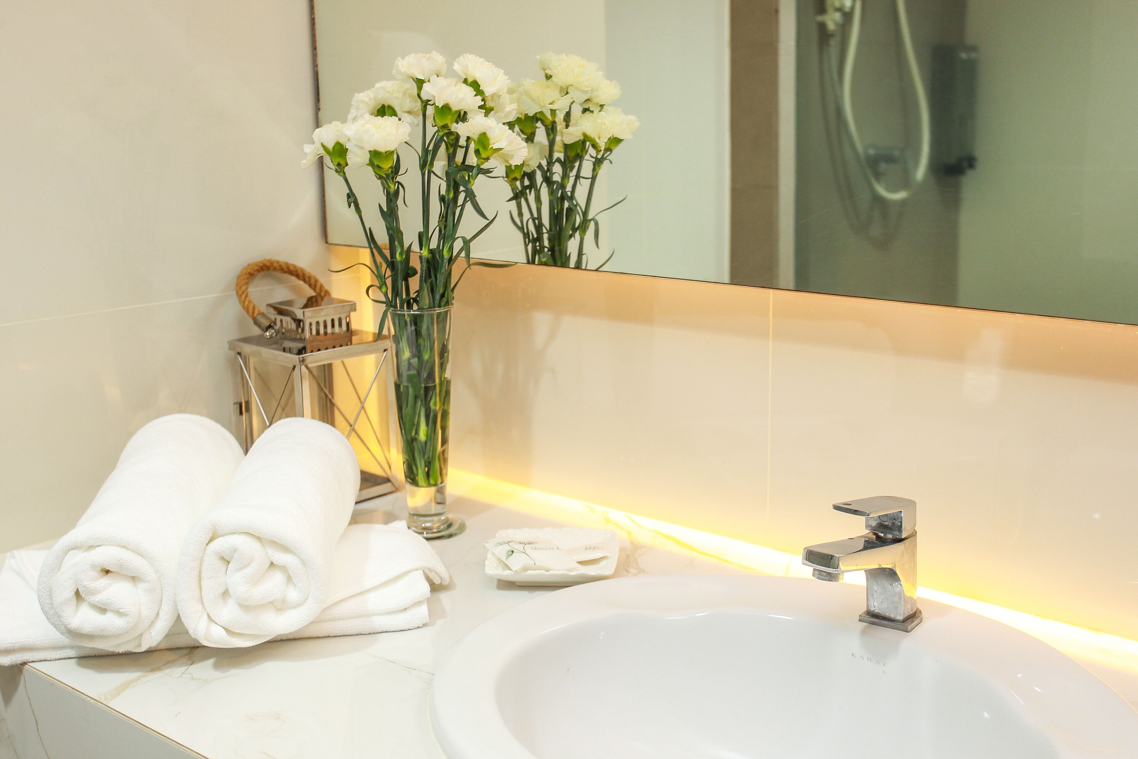 A bathroom with a white sink, a mirror, and a vase with white flowers.