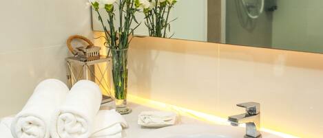 A bathroom with a white sink, a mirror, and a vase with white flowers.