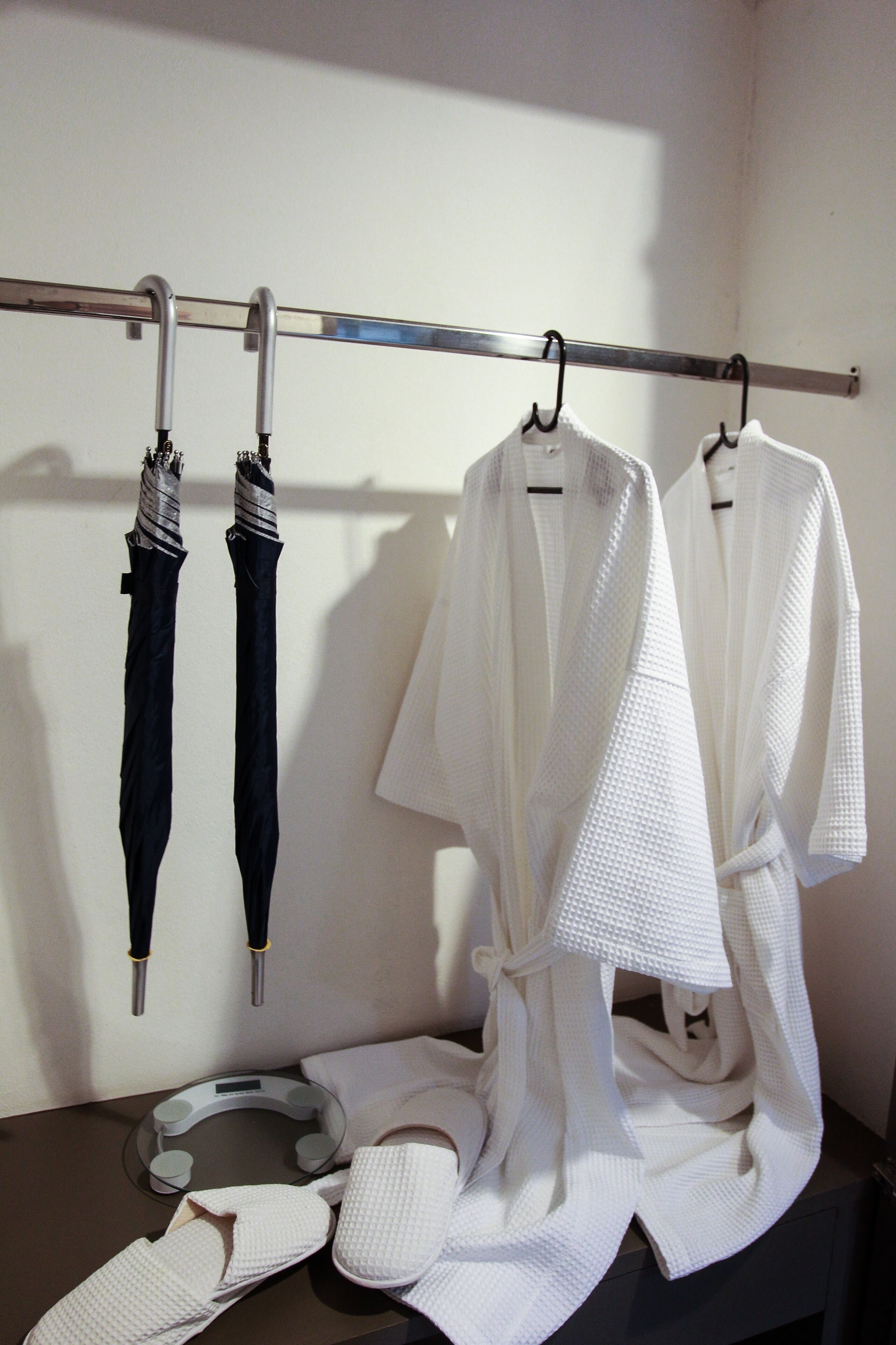 A bathroom with a towel rack holding two white robes and two umbrellas.