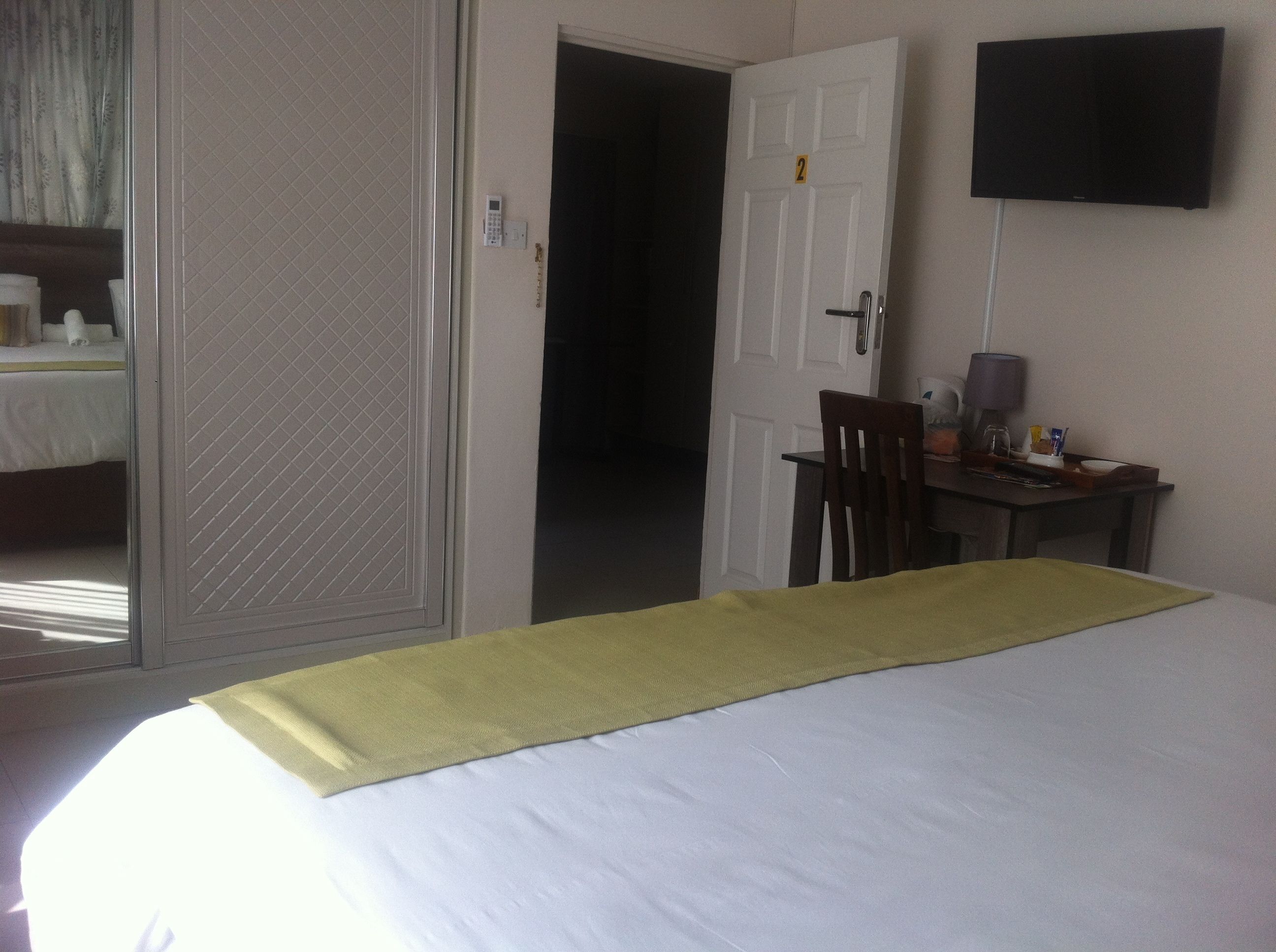Habitación de hotel con cama, escritorio con silla, televisor montado en la pared y puerta que da a otra habitación.