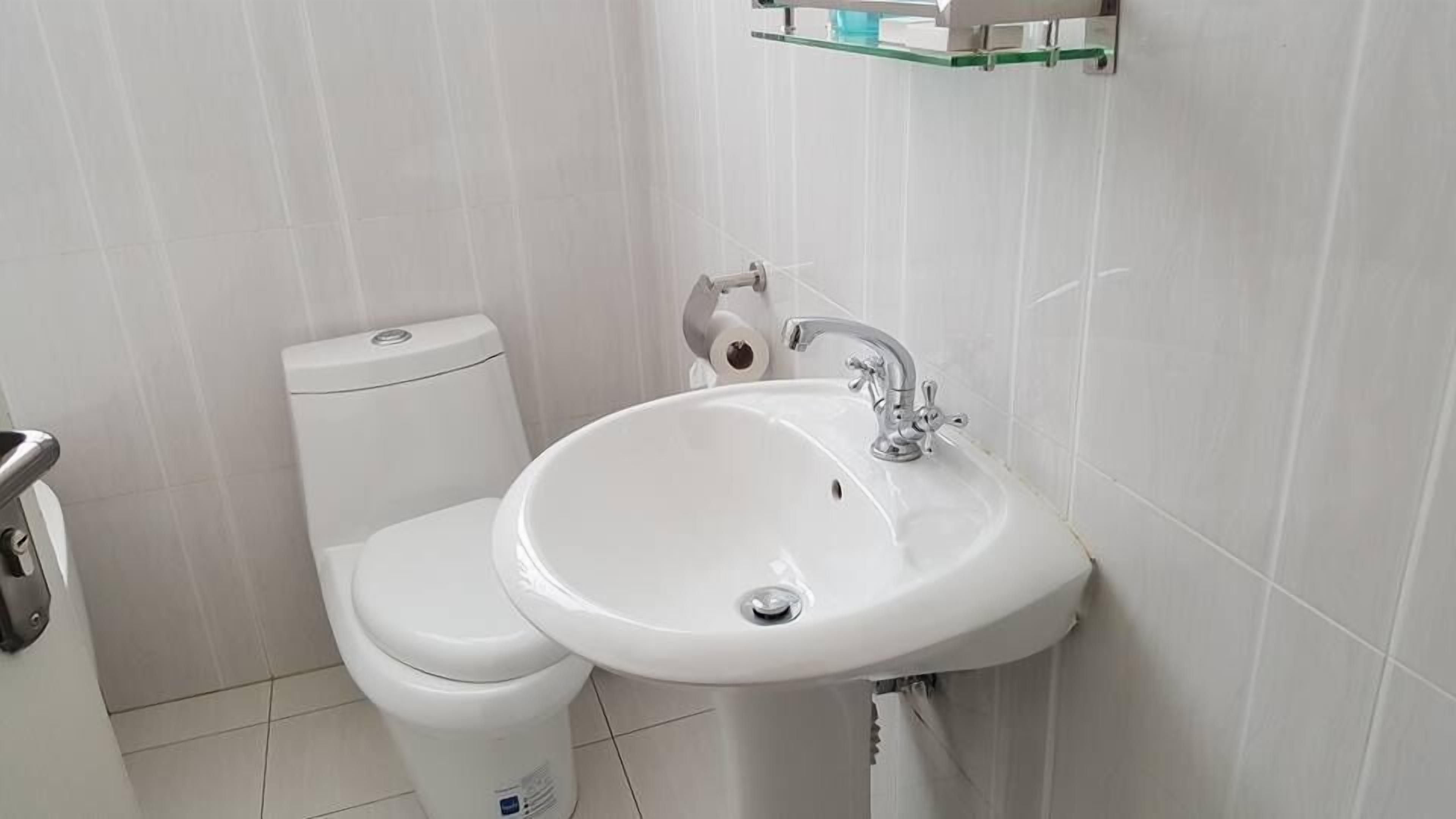 Een badkamer met een wit toilet, een witte wastafel en een glazen plank boven de wastafel.
