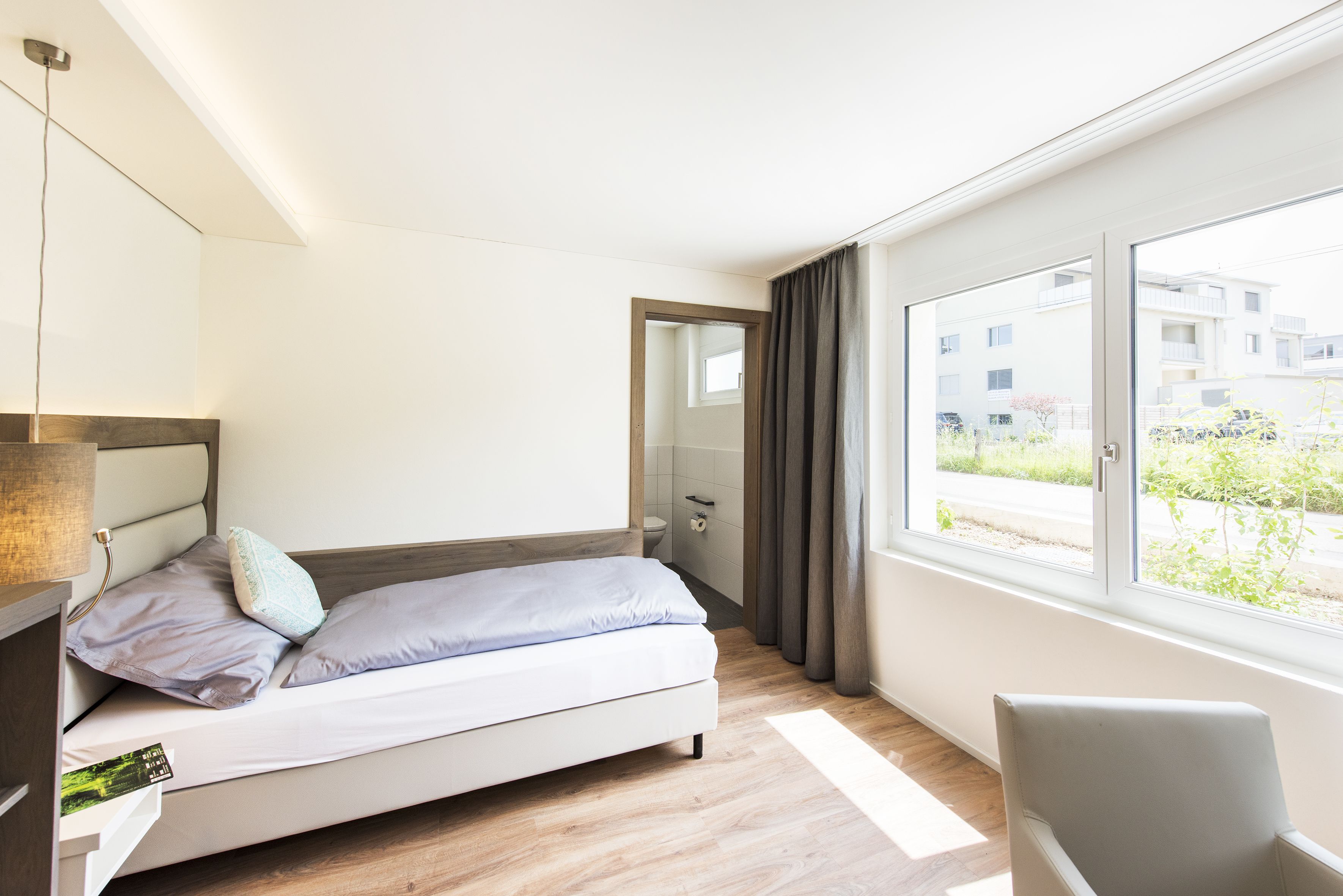 Un dormitorio moderno con cama, mesita de noche y un amplio ventanal con cortinas.