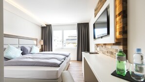 A modern hotel room with a bed, a desk, a flat-screen TV, and a window with curtains. - Hotel Tilia (Uster)