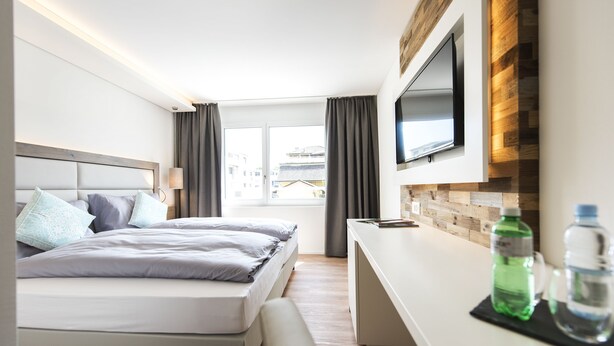 Una habitación de hotel moderna con cama, escritorio, televisor de pantalla plana y ventana con cortinas.